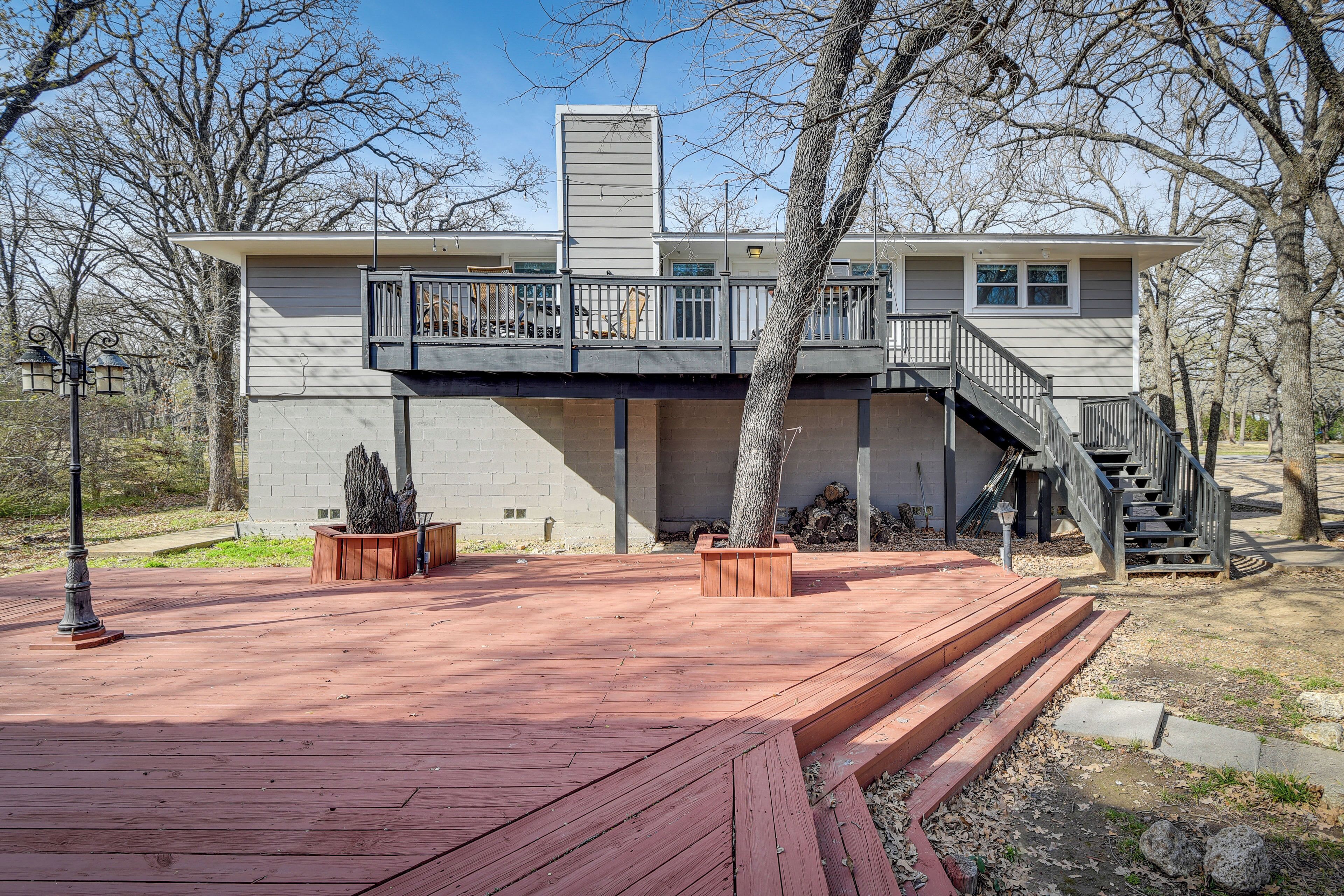 A two-story house with a wooden deck, a staircase, and a large tree in front.