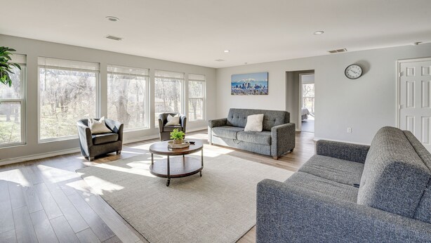 A spacious living room with large windows, a gray sofa, a round coffee table, and a gray armchair. - Modern Flower Mound Home < 2 Mi to River Walk (Flower Mound)
