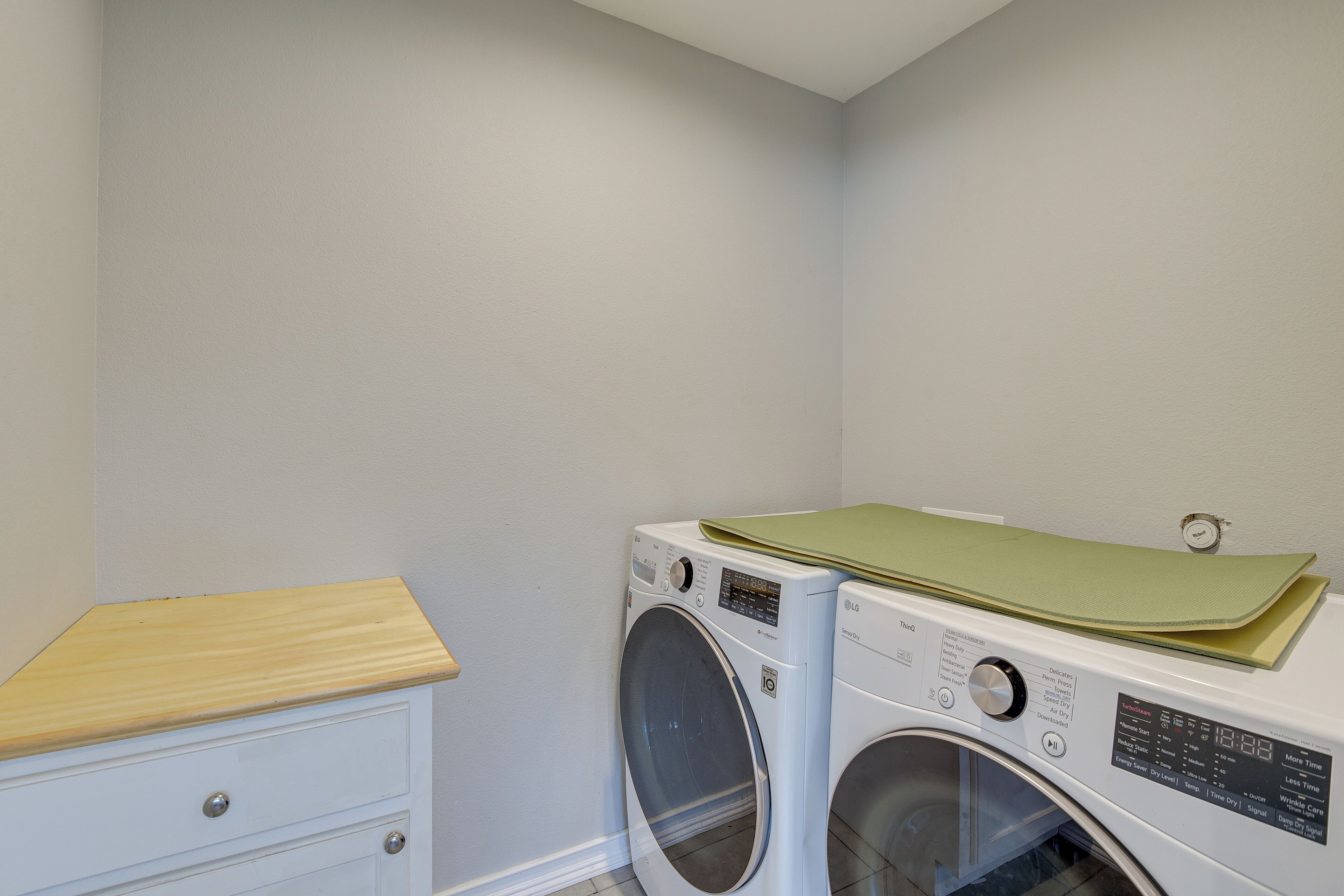 Une buanderie équipée d’un lave-linge et d’un sèche-linge, d’une armoire en bois et d’un tapis vert posé sur le sèche-linge.