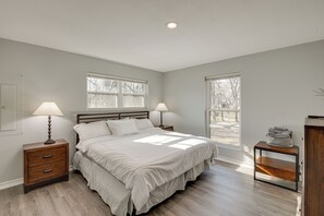 A bedroom with a bed, two bedside tables with lamps, a wooden bench, and two windows. - Modern Flower Mound Home < 2 Mi to River Walk (Flower Mound)