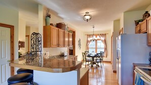 A kitchen with wooden cabinets, a marble island with bar stools, a refrigerator, and a dining area with a table and chairs. - Scenic Views & Trail Access! Blue Ridge Mtns Condo (Burnsville)