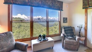 A room with two patterned armchairs, a small ottoman, and a view of a forested landscape through large windows. - Scenic Views & Trail Access! Blue Ridge Mtns Condo (Burnsville)