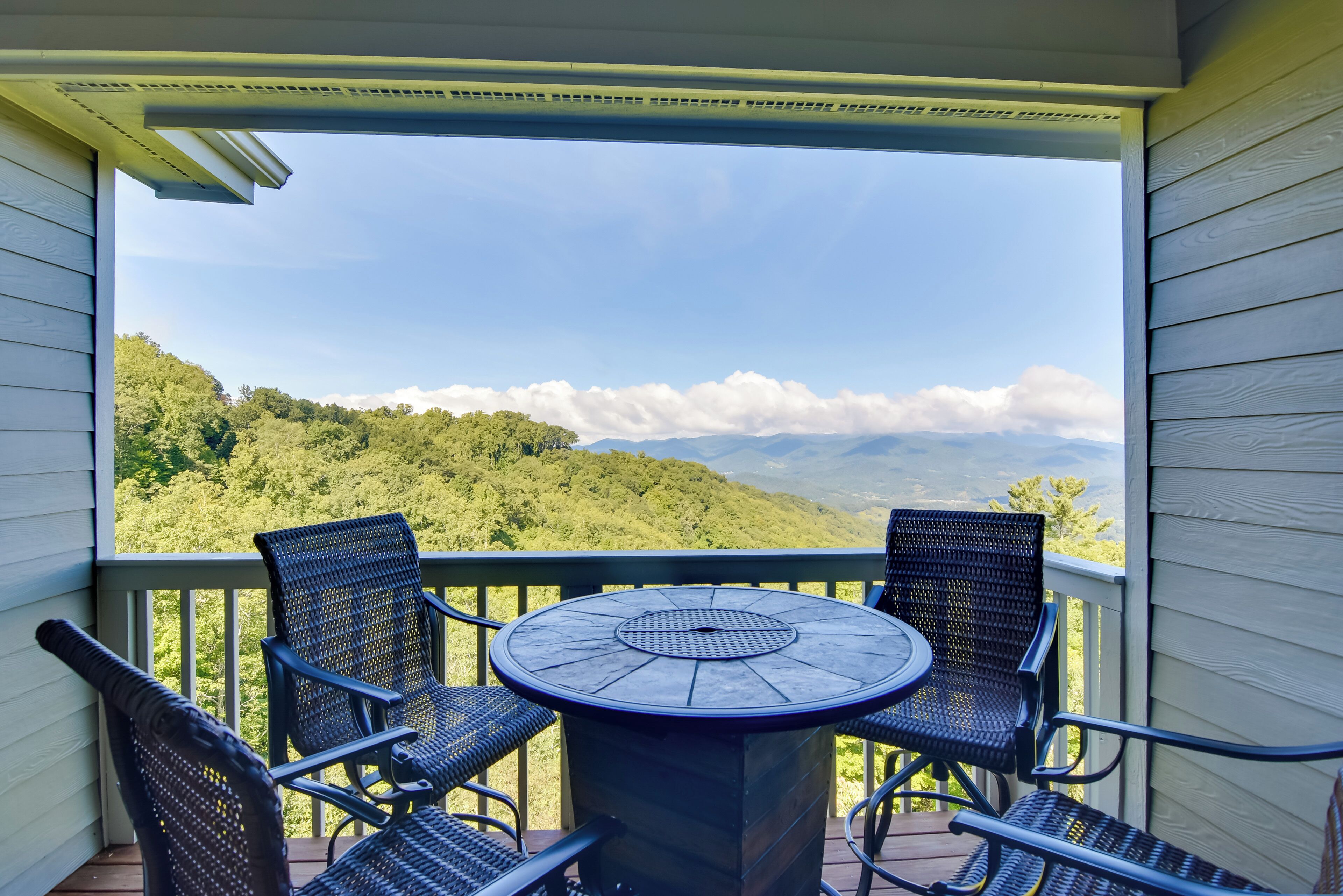 A balcony with a table and four chairs, overlooking a mountainous landscape.