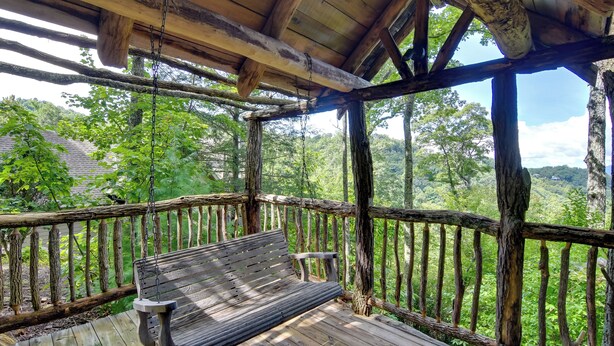 A wooden deck with a bench and a table, surrounded by a rustic wooden railing, overlooking a lush green landscape. - Scenic Views & Trail Access! Blue Ridge Mtns Condo (Burnsville)