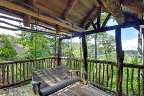A wooden deck with a bench and a table, surrounded by a rustic wooden railing, overlooking a lush green landscape. - Scenic Views & Trail Access! Blue Ridge Mtns Condo (Burnsville)