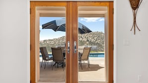 En skydedør, der fører ud til en udendørs terrasse med pool og stole.