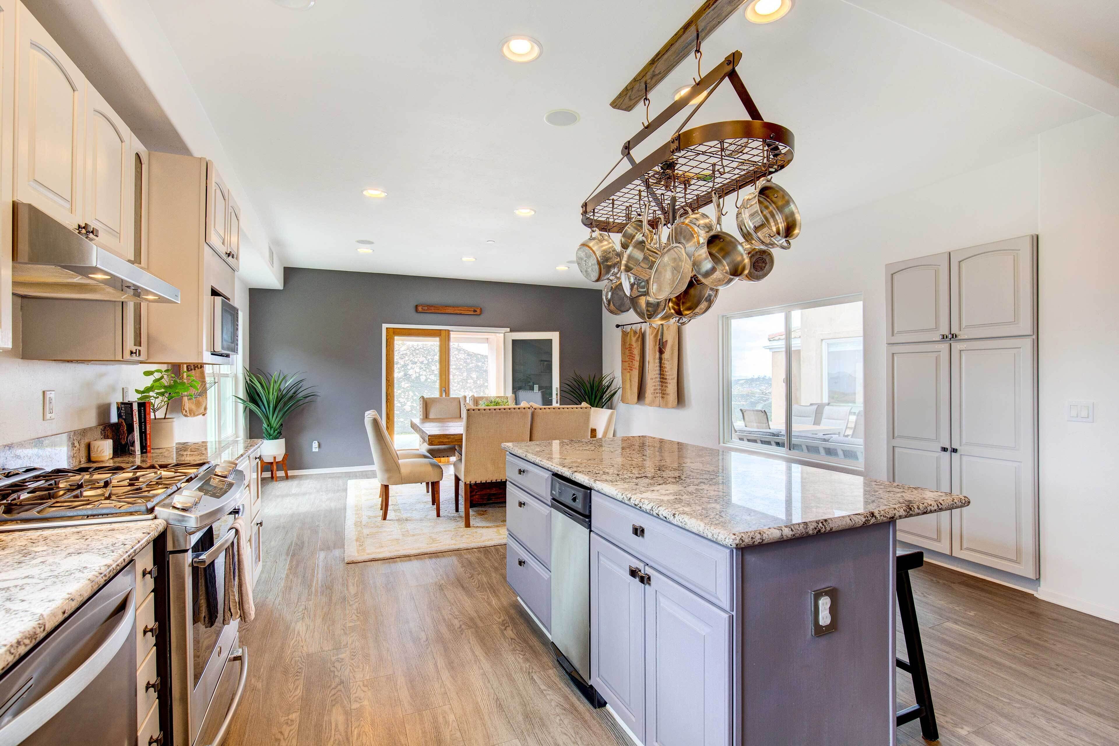 A modern kitchen with granite countertops, stainless steel appliances, and a hanging pot rack.