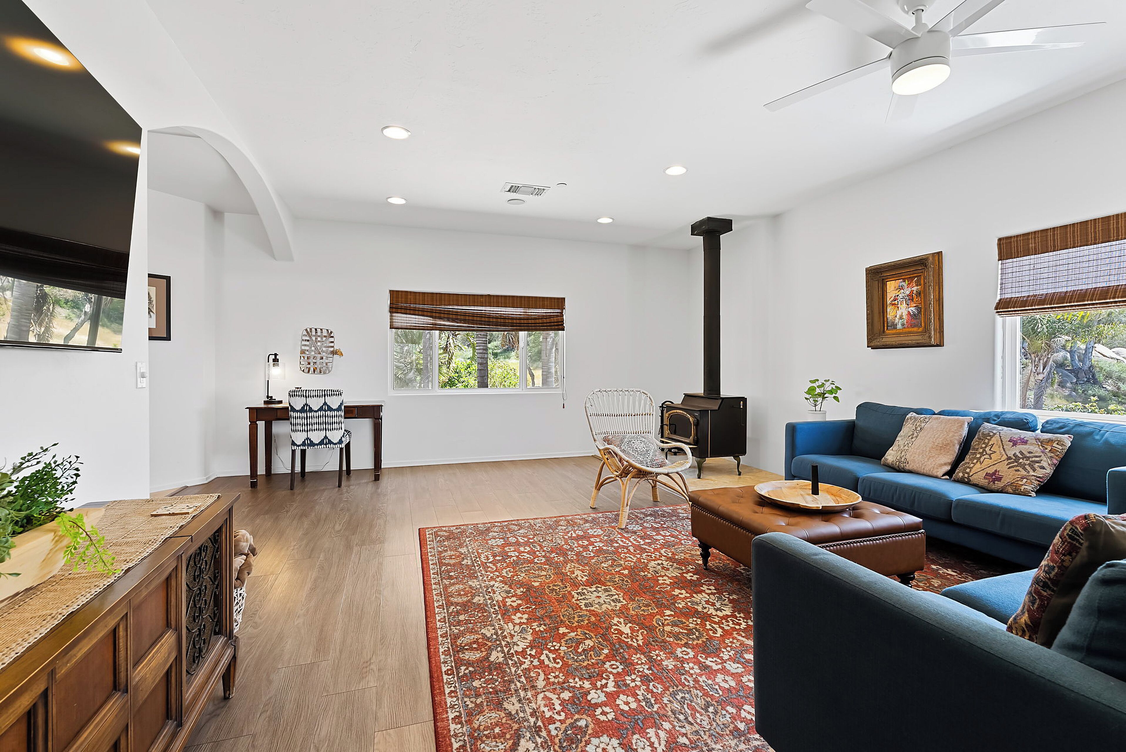A living room with a blue sofa, a wooden coffee table, a patterned rug, a wooden cabinet, and a white ceiling fan.
