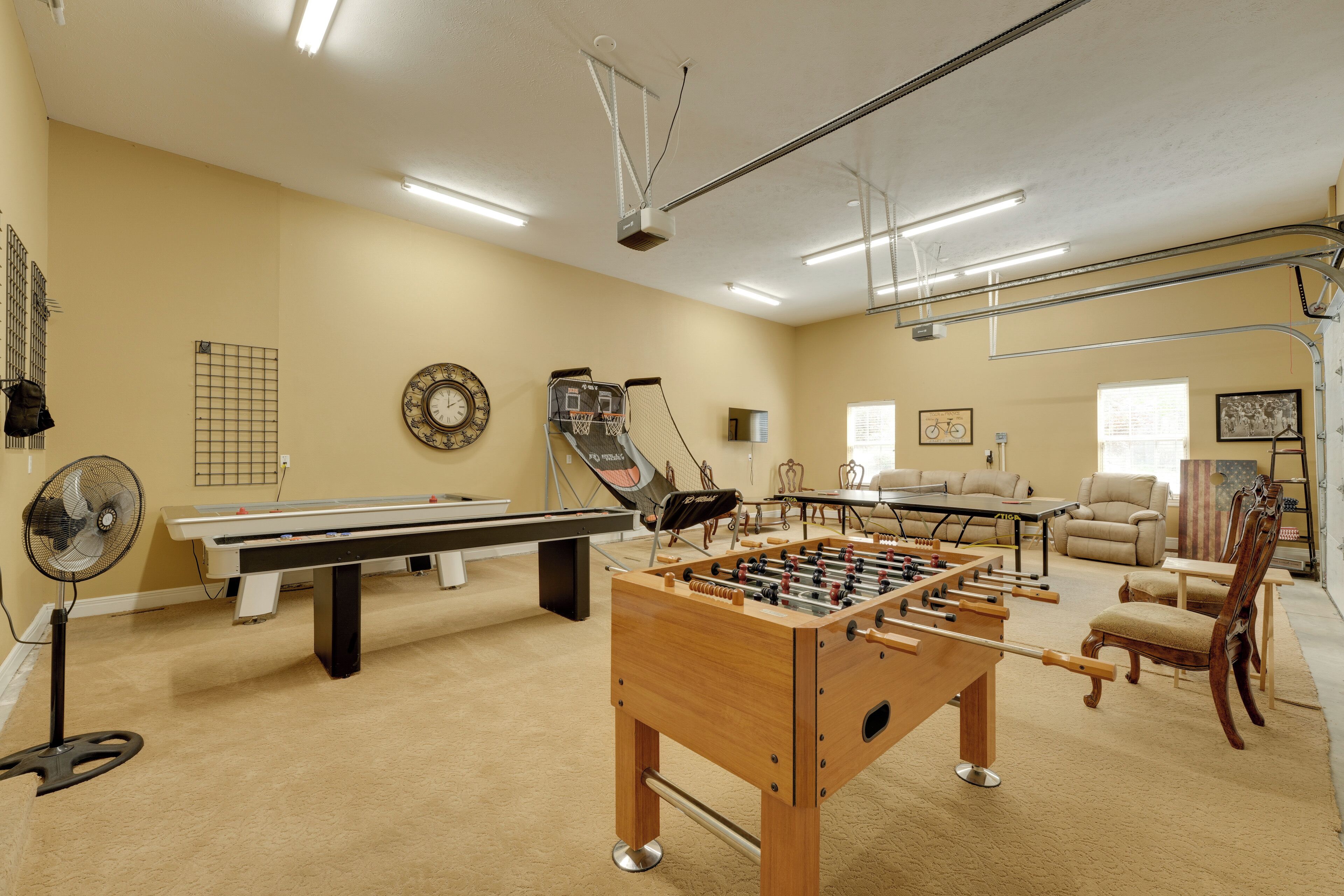 A room with a foosball table, pool table, and a fan.
