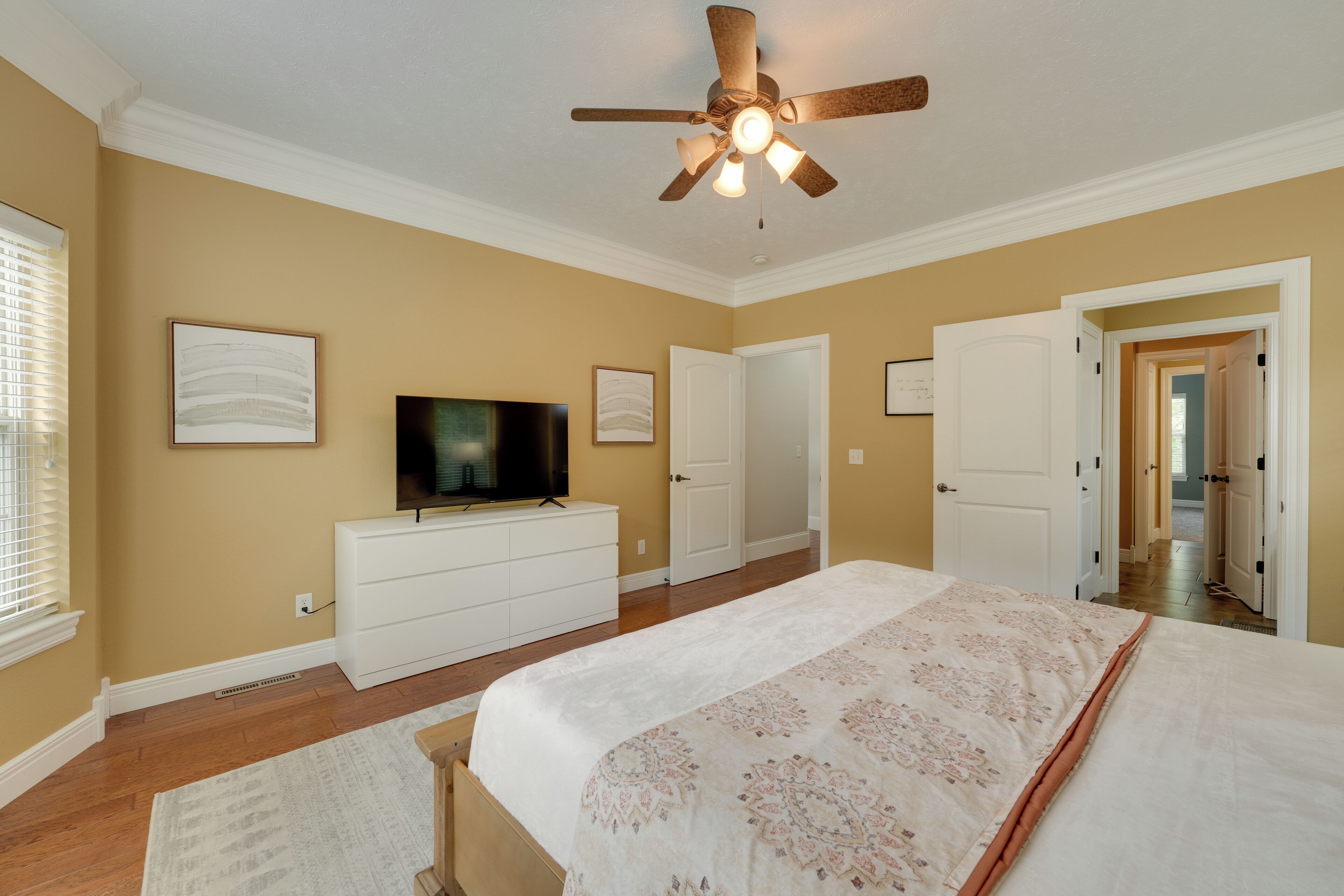 Une chambre à coucher avec un lit, un ventilateur de plafond, une télévision et une commode.
