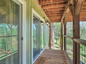 A covered porch with a wooden railing, a welcome mat, and a view of the surrounding forest. - Luxury Retreat: Custom Mi-wuk Village Cabin! (Mi-Wuk Village)