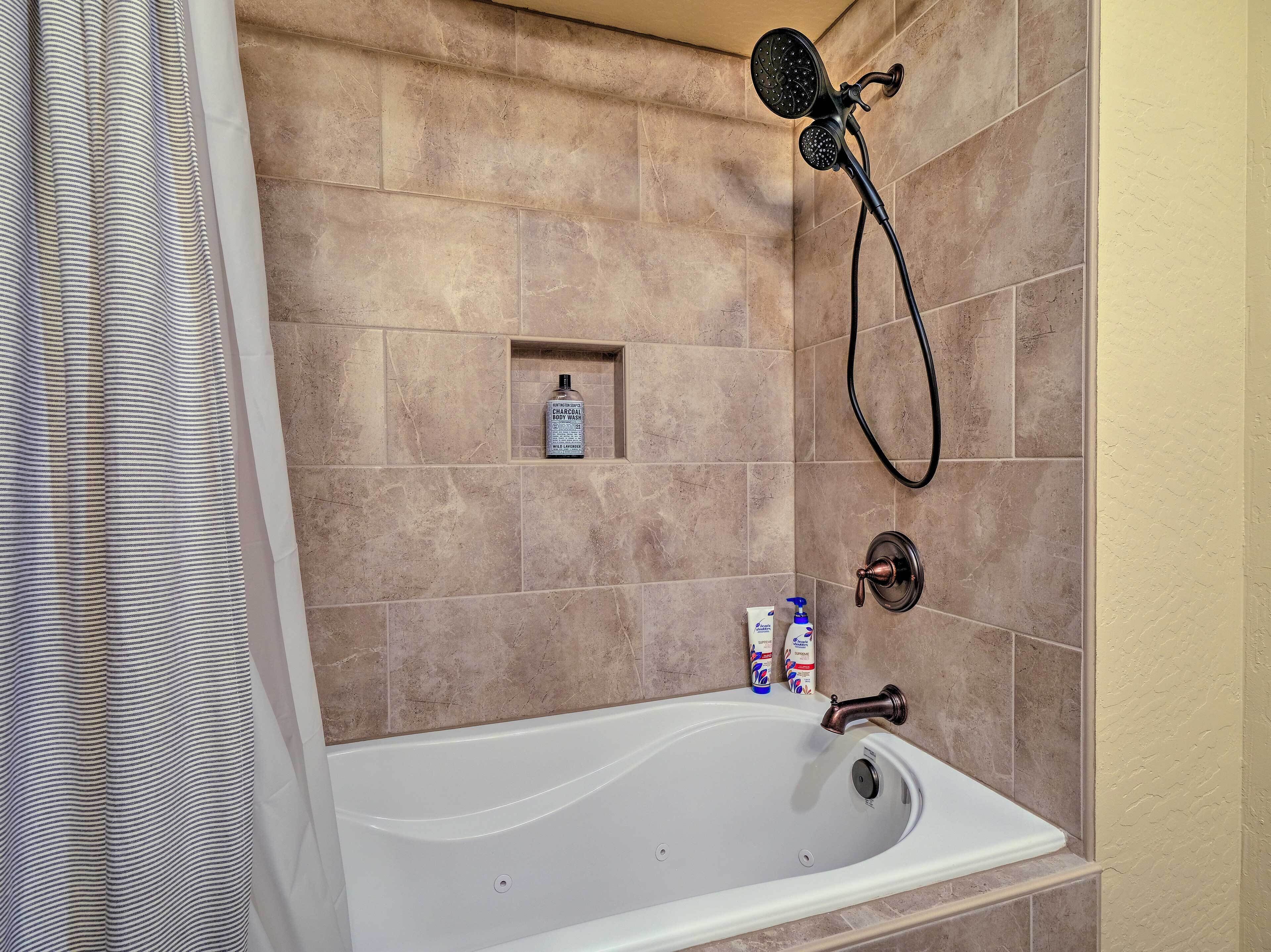 A bathroom with a bathtub, a showerhead, and toiletries.