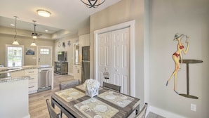 A modern kitchen with white cabinets, a dining area with a wooden table, and a decorative wall piece. - Ocean Isle Beach Home w/ Shared Lanai & Grill (Ocean Isle Beach)