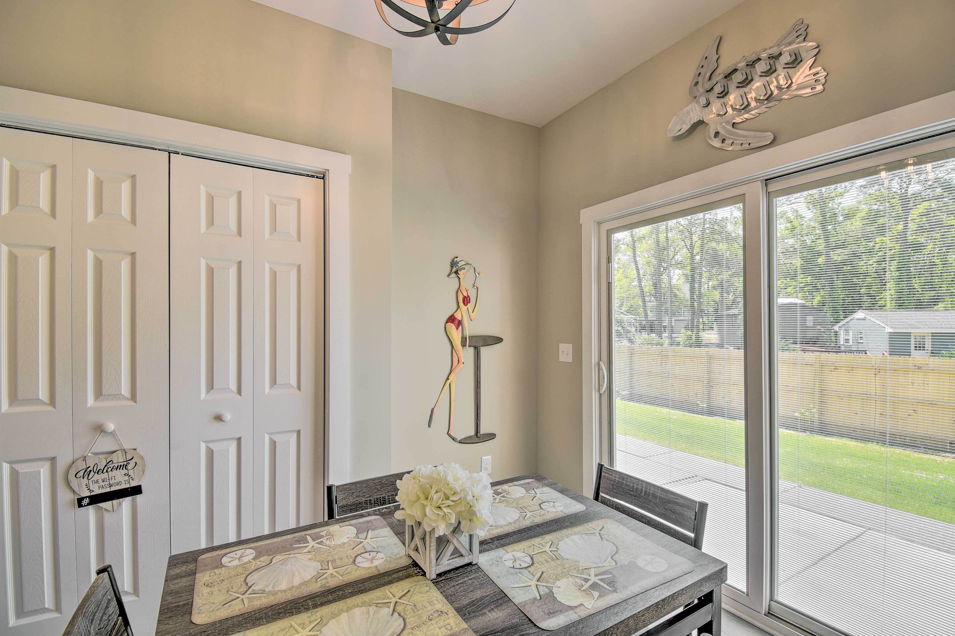 A dining area with a table set for four, a decorative wall piece, and a view of the backyard through large sliding glass doors.