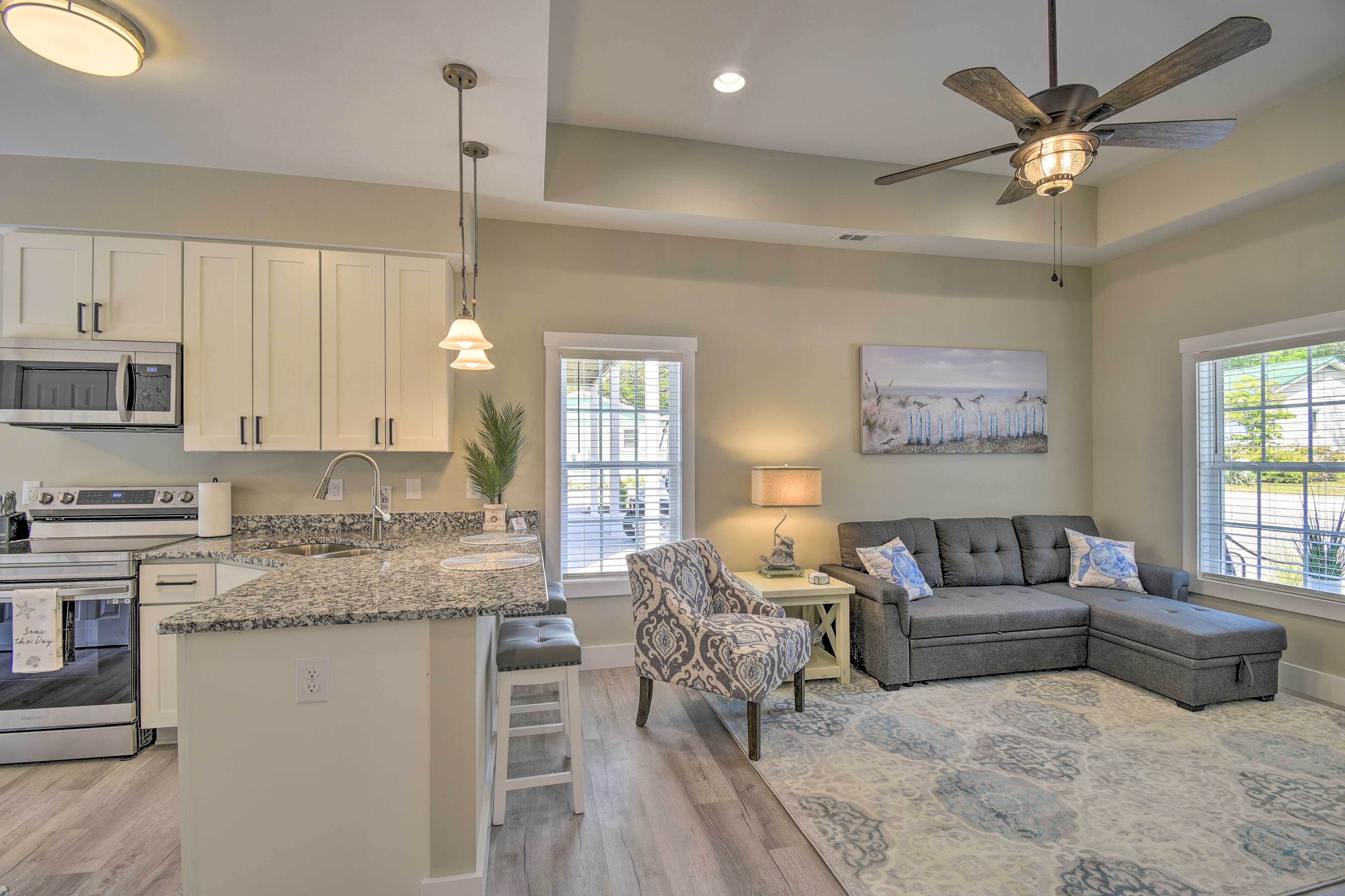 A modern kitchen with built-in appliances, a dining area with a patterned chair, and a living room with a sectional sofa.