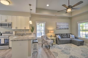 A modern kitchen with built-in appliances, a dining area with a patterned chair, and a living room with a sectional sofa. - Ocean Isle Beach Home w/ Shared Lanai (Ocean Isle Beach)