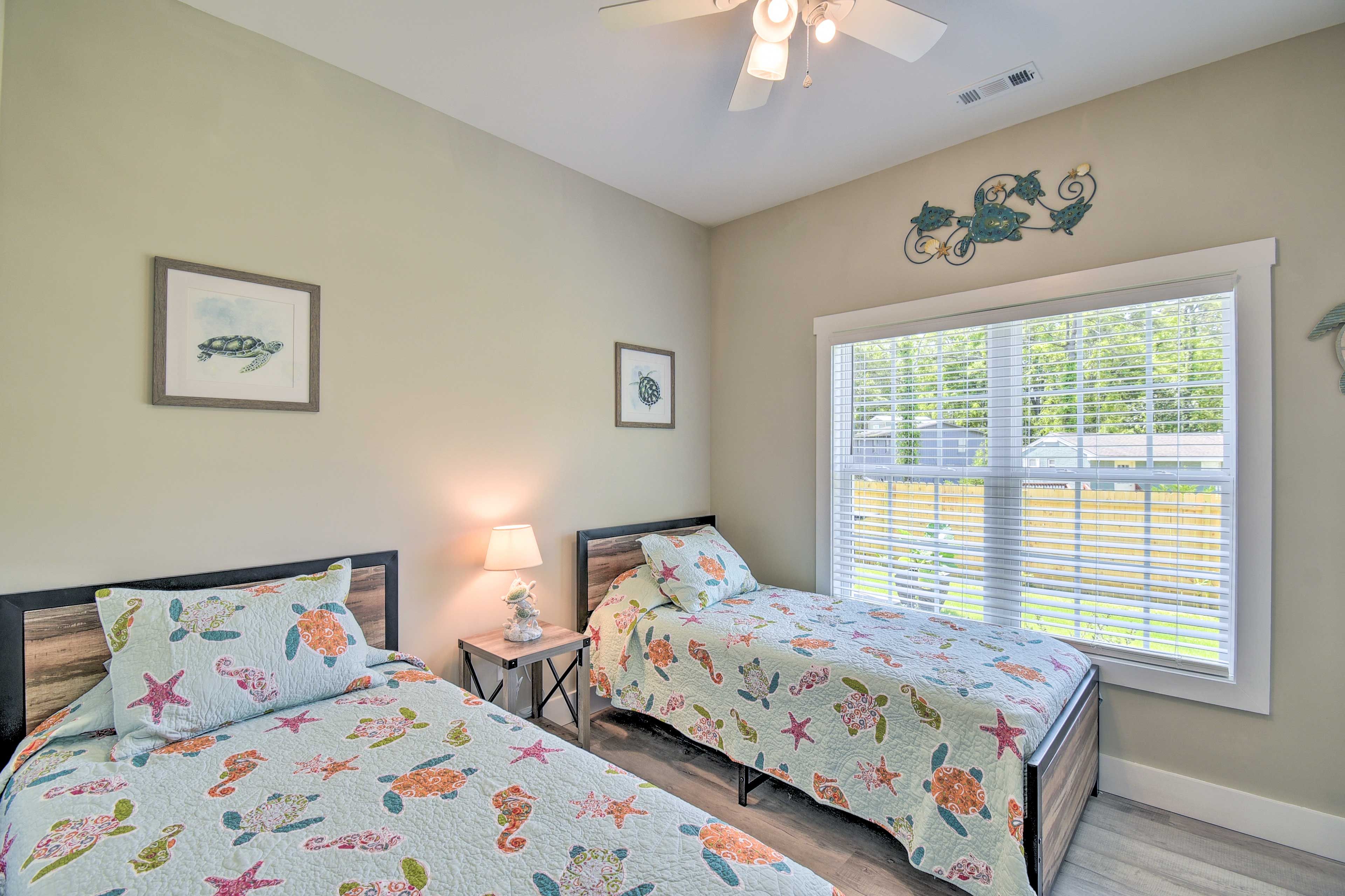 A bedroom with two beds, a ceiling fan, and a window with blinds.