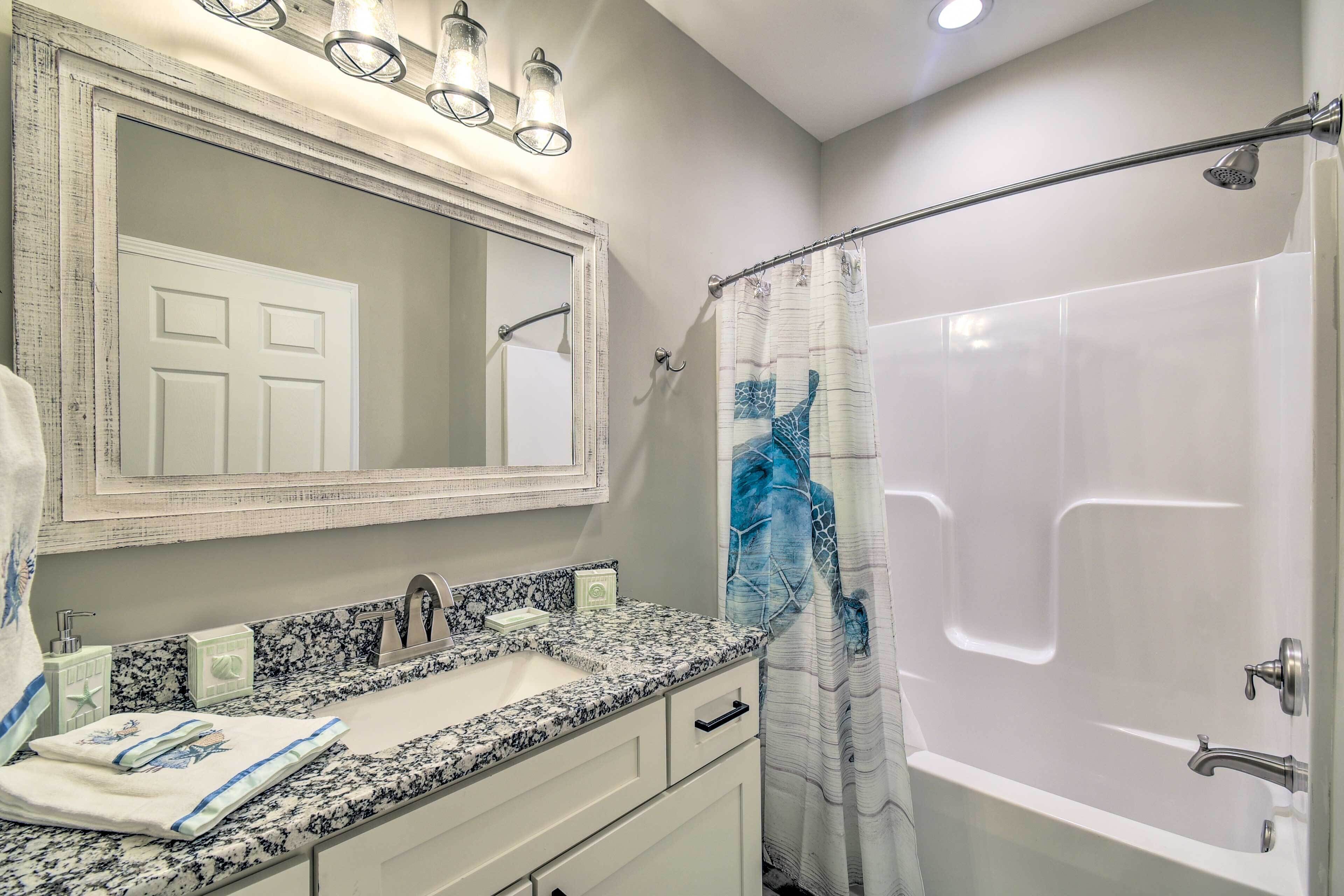 A bathroom with a marble sink, a large mirror, a shower with a blue curtain, and a ceiling light fixture.