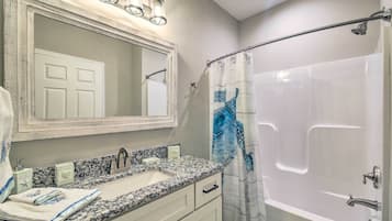 Une salle de bain avec un lavabo en marbre, un grand miroir, une douche avec un rideau bleu et un luminaire au plafond.