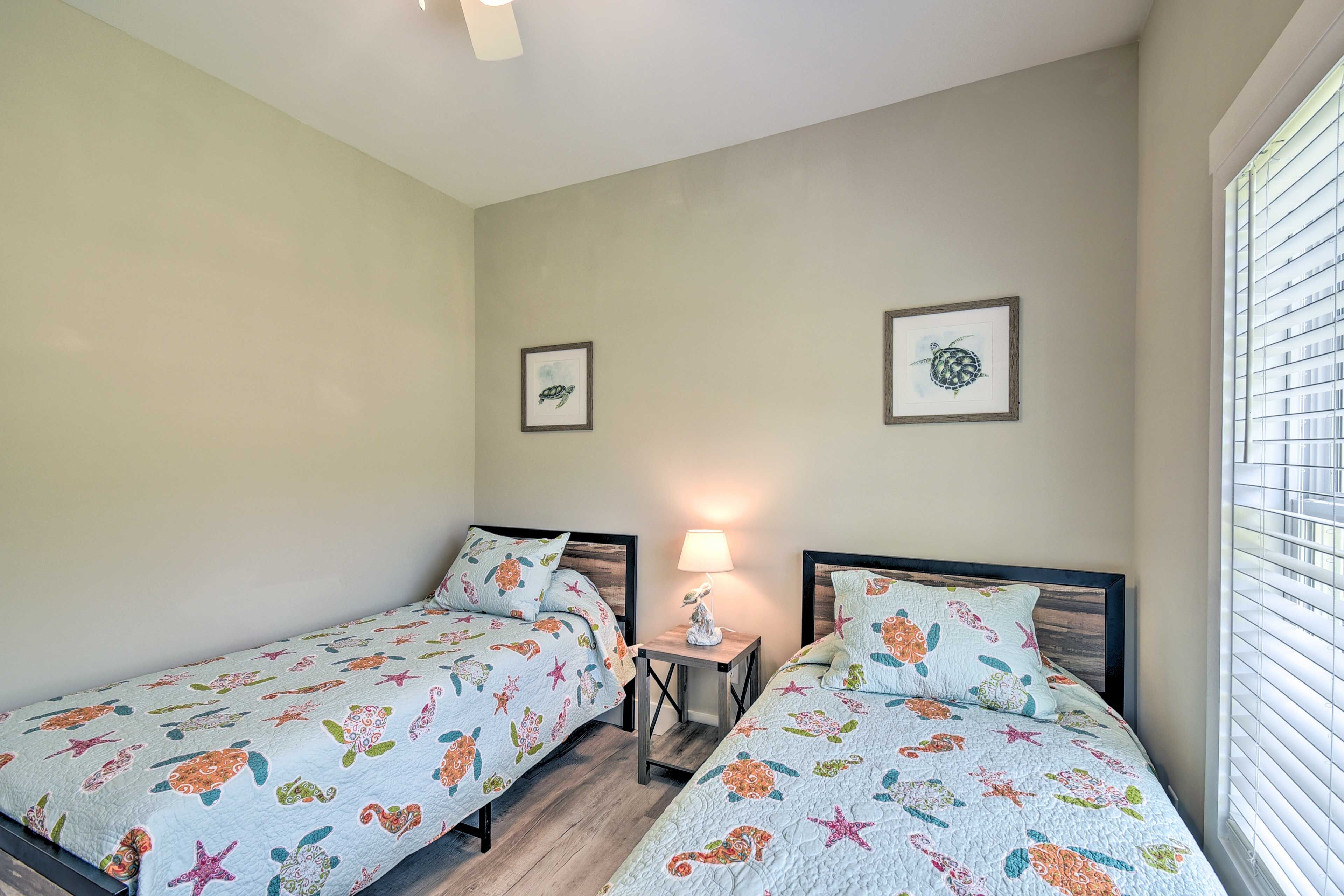 A bedroom with two single beds, each with a floral-patterned bedspread, a bedside table with a lamp, and framed pictures on the wall.