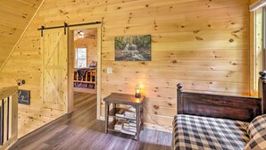 Ein gemütliches Blockhaus-Interieur mit Holzausstattung, einem Bett mit karierter Bettwäsche, einem kleinen Tisch mit Lampe und einem Wandbild einer Wasserfall.
