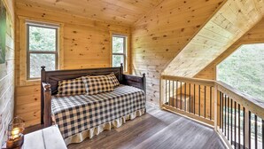 Ein Schlafzimmer einer Holzhütte mit kariertem Bett, zwei Fenstern und einem Balkon mit Geländer.