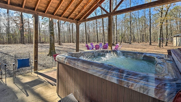 Eine Holzterrasse mit Whirlpool, umgeben von Bäumen und Gartenmöbeln.