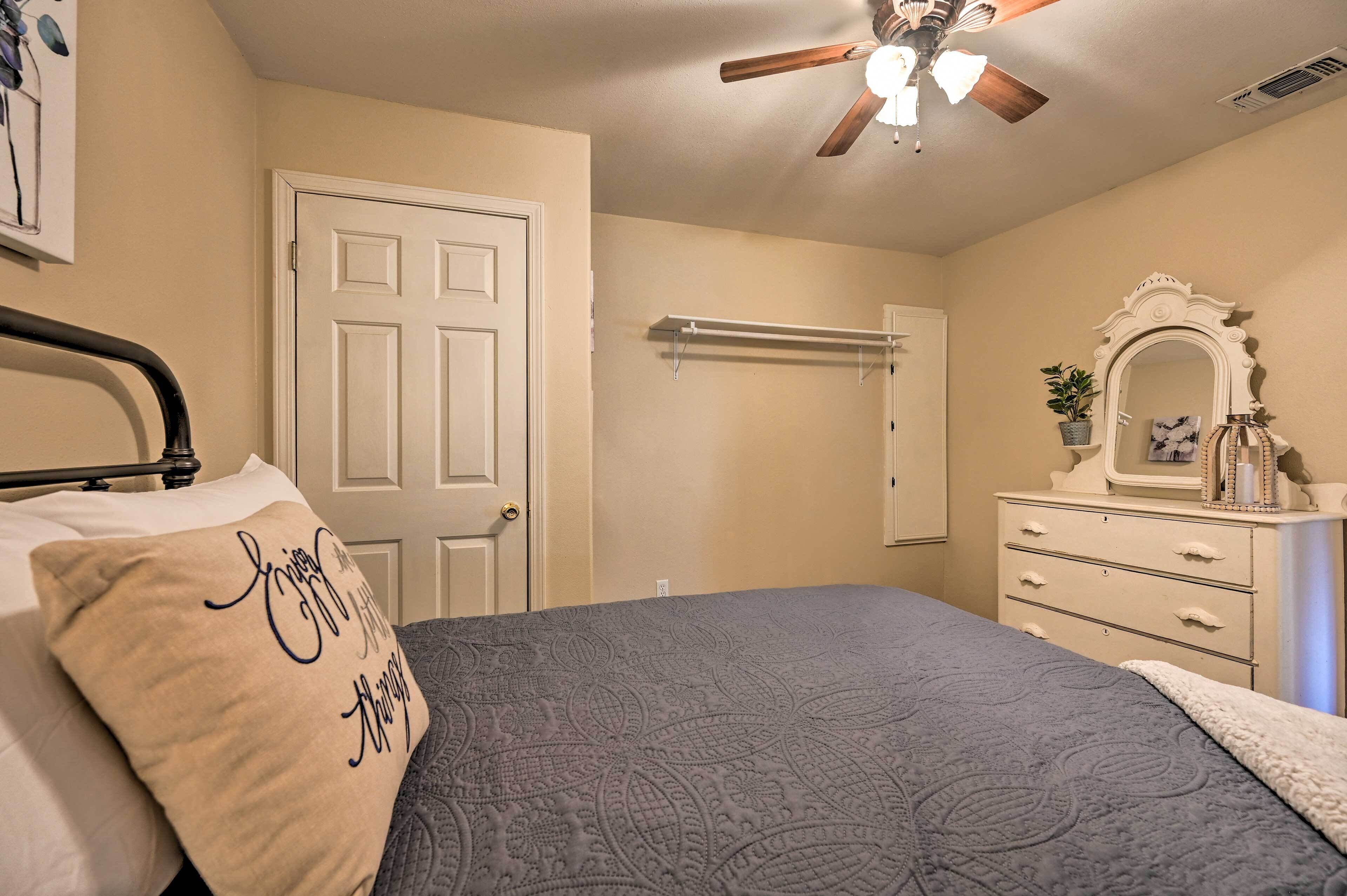 A bedroom with a bed, a dresser, a mirror, a ceiling fan, and a door.