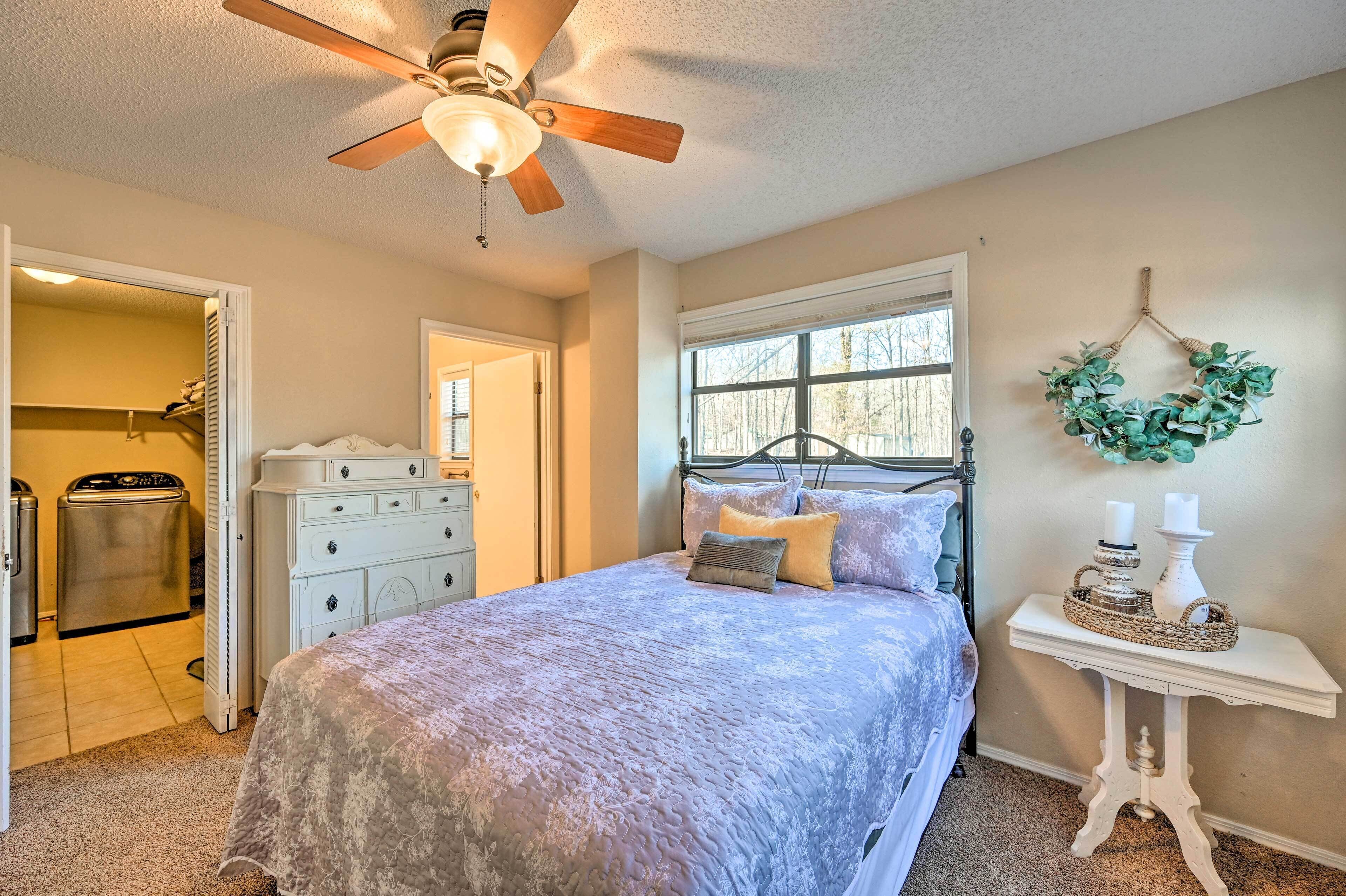 A bedroom with a bed, a ceiling fan, a dresser, a window, and a wall-mounted wreath.