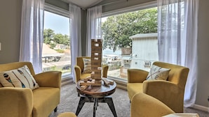 A room with two yellow armchairs, a round table with wooden blocks, and large windows with white curtains. - Osage Beach Family Hideaway on No-wake Cove! (Osage Beach)