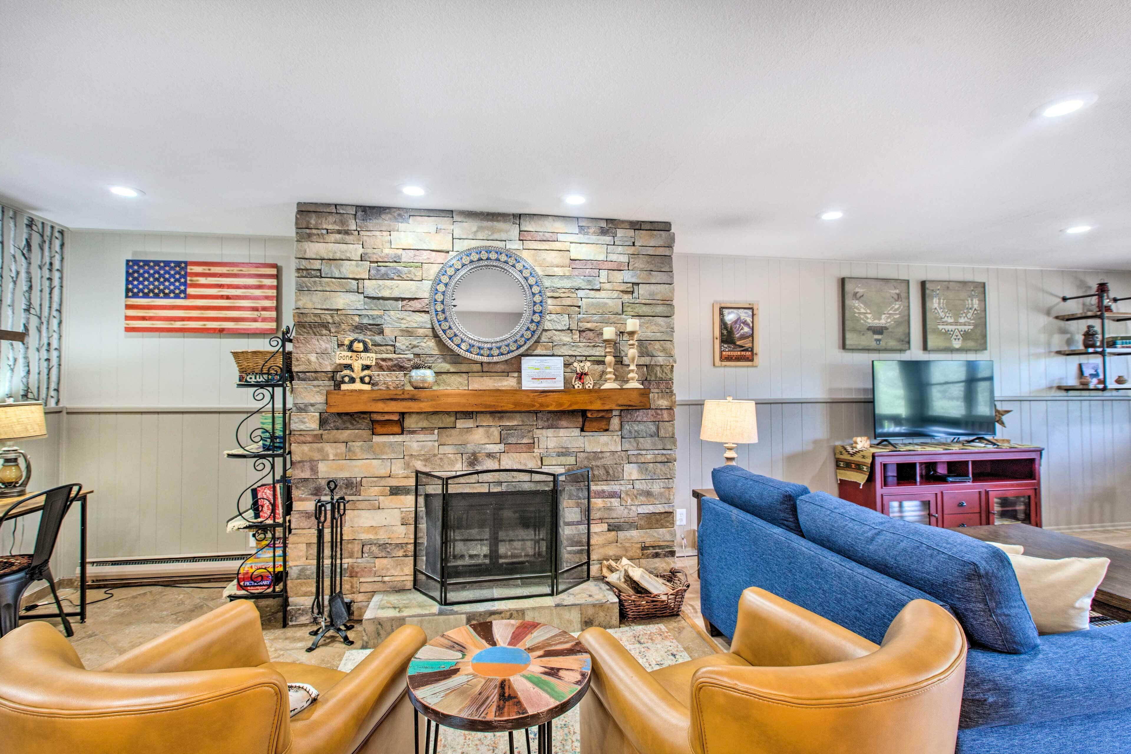 A living room with a stone fireplace, a blue sofa, leather chairs, and a television.