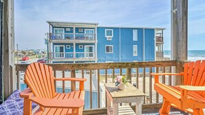 A wooden deck with two orange Adirondack chairs and a small table with a vase of flowers. A blue building with balconies is visible in the background.