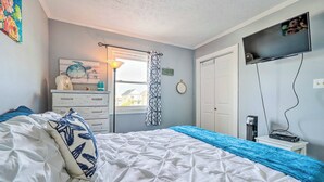 A bedroom with a bed, a dresser, a TV, and a window with curtains.