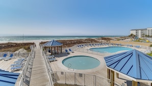 A beachside resort with multiple swimming pools, lounge chairs, and a wooden deck leading to the beach.