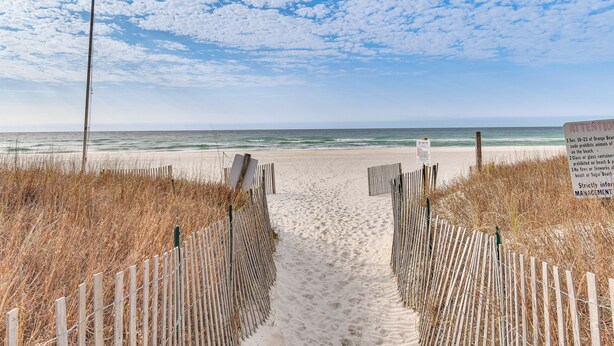 A sandy beach path with wooden fences and a signboard.