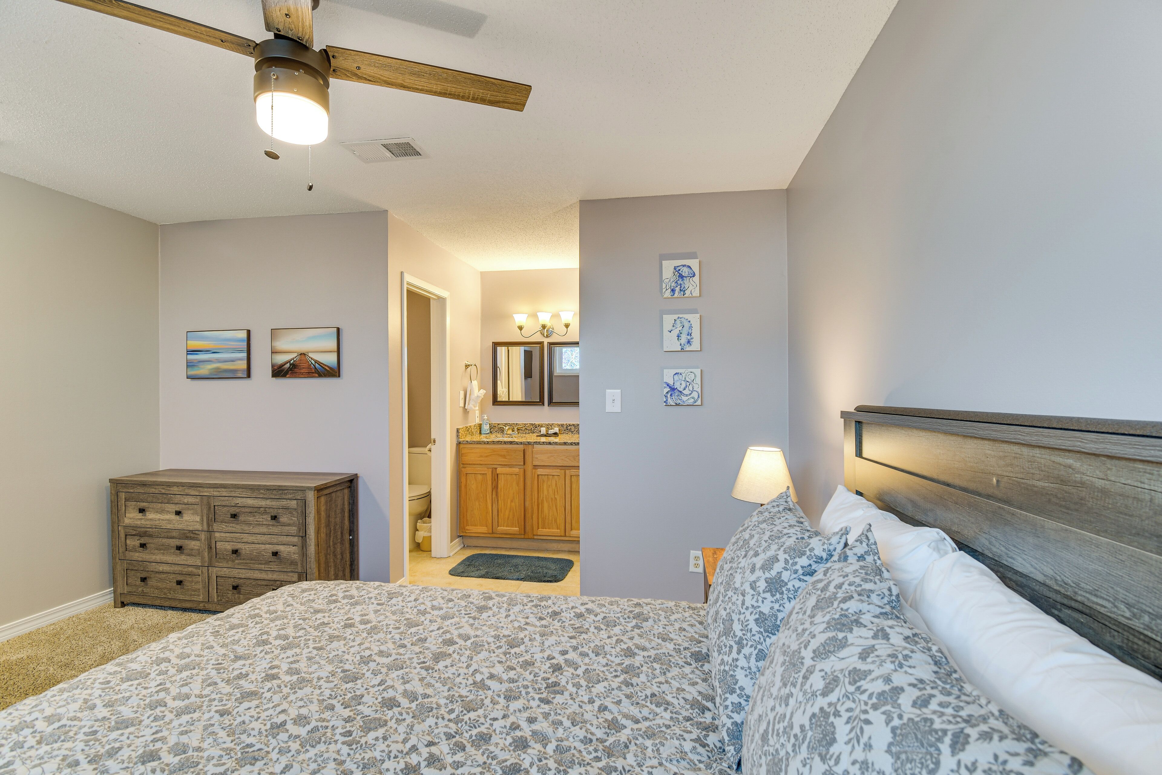 Une chambre avec un lit, une commode, un ventilateur de plafond et une vue sur la cuisine.