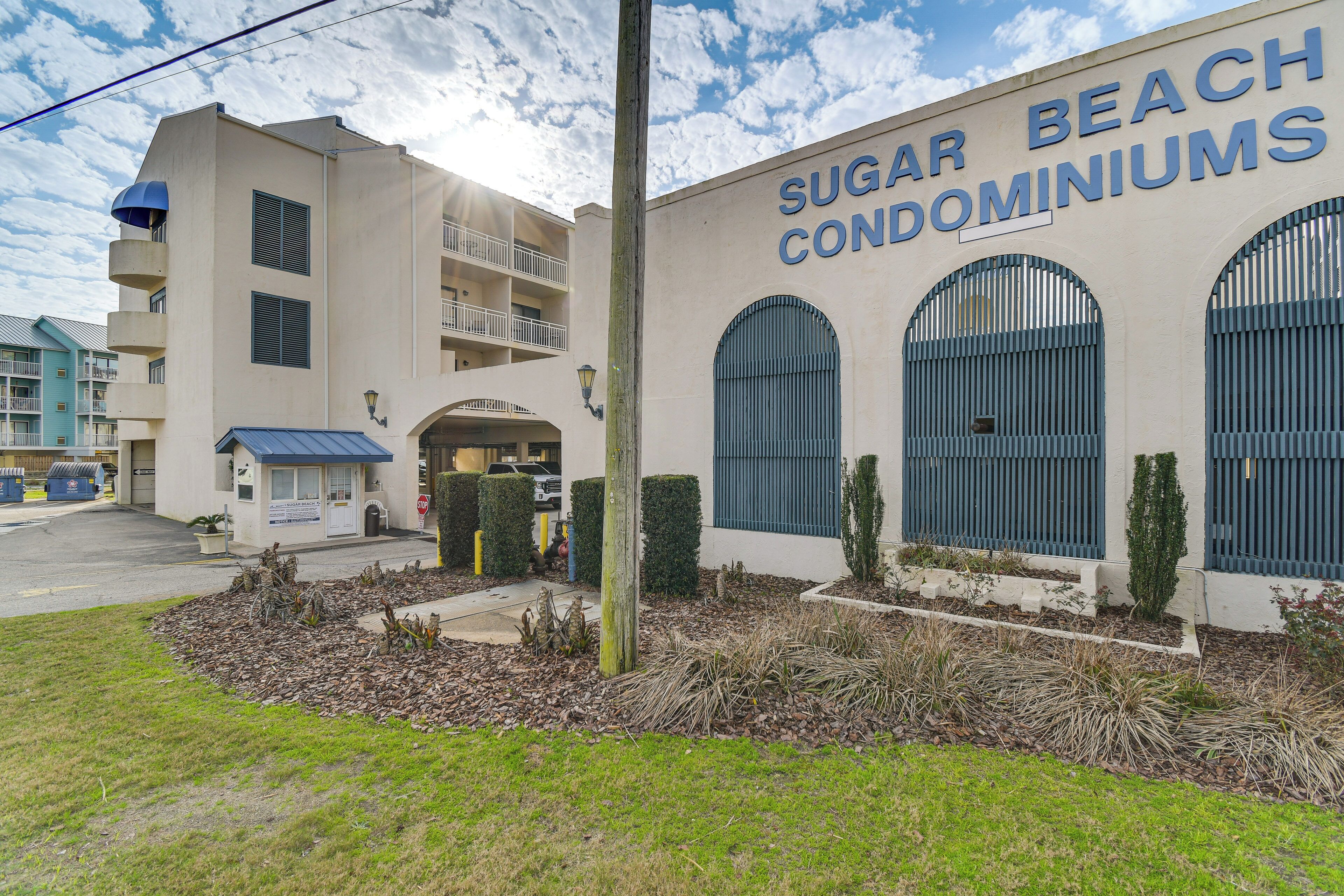 A building labeled "Sugar Beach Condominiums" with a flat roof, multiple balconies, and a gated entrance.