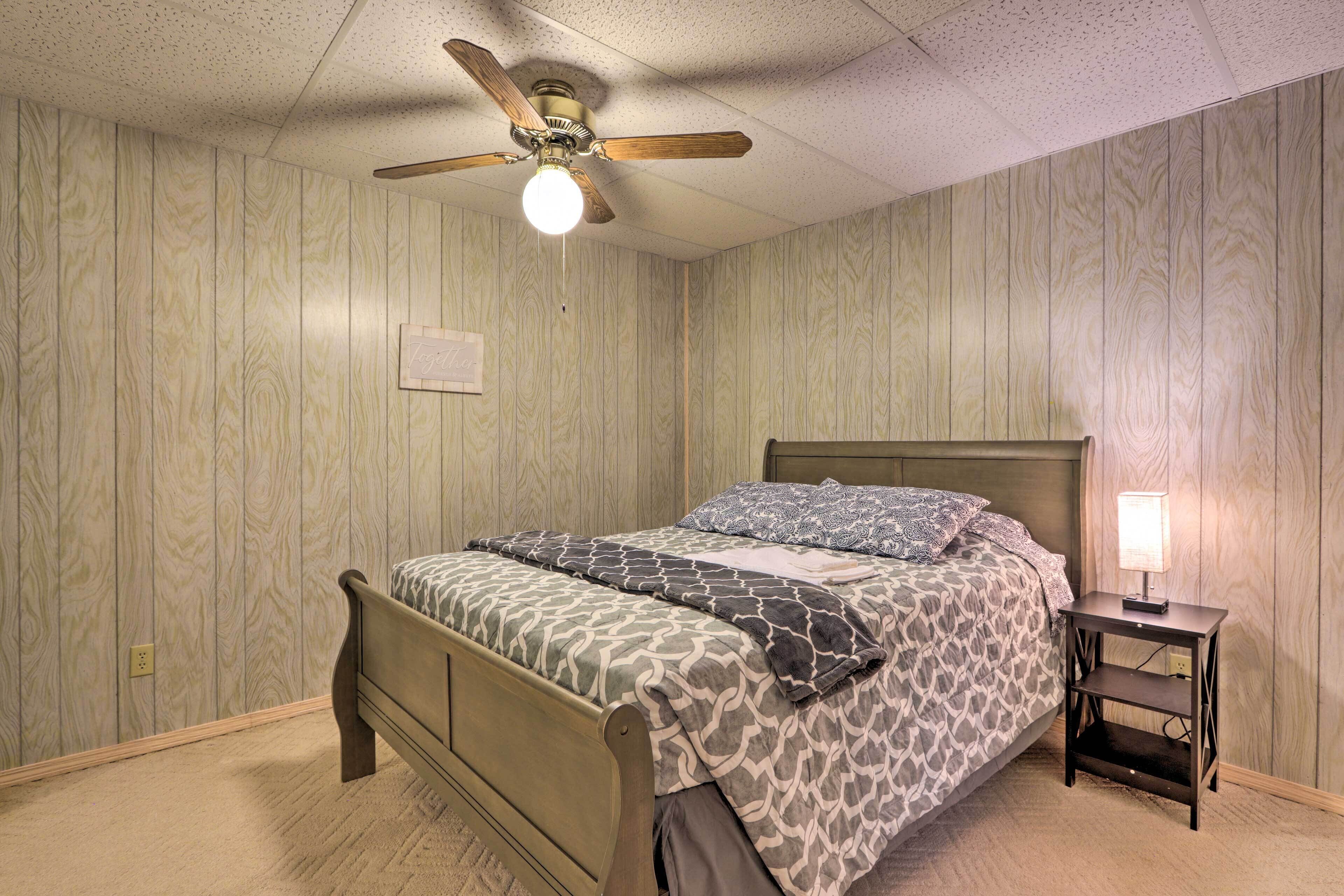 A bedroom with a wooden bed, a nightstand with a lamp, and a ceiling fan.
