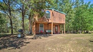 A rustic cabin with a large window, a porch, and a gas tank outside. - Peaceful 'black Fork Cabin 1' - Fish On-site! (Nashoba)
