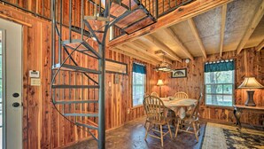 A wooden interior with a spiral staircase, a dining area with chairs and a table, and windows with curtains. - Peaceful 'black Fork Cabin 1' - Fish On-site! (Nashoba)