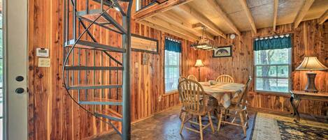 A wooden interior with a spiral staircase, a dining area with chairs and a table, and windows with curtains.