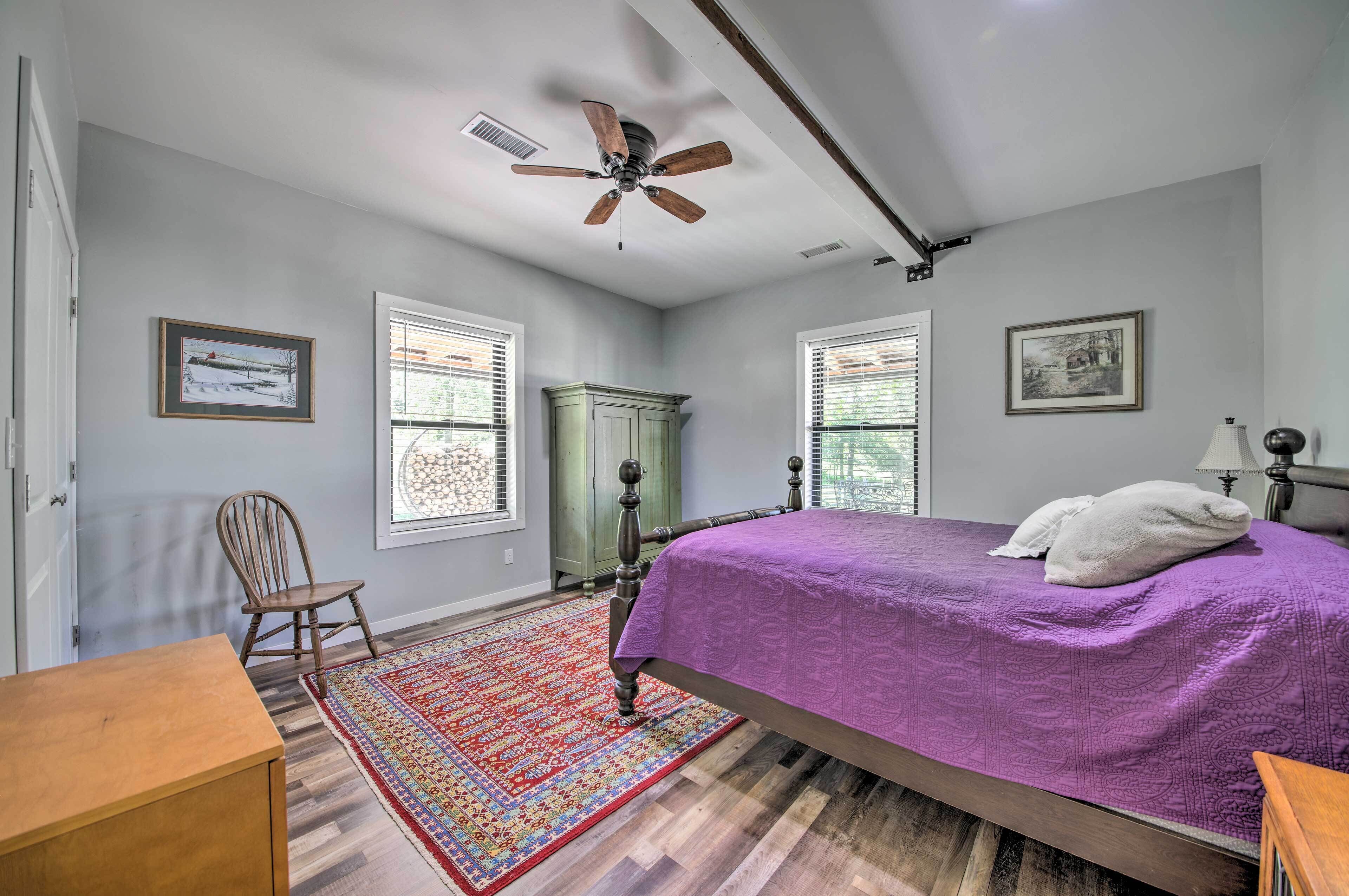 A bedroom with a bed, a chair, a wooden dresser, a ceiling fan, and a window with blinds.