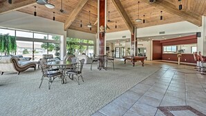 Un hall d’entrée spacieux avec un haut plafond en bois, une table de billard, des sièges confortables et de grandes fenêtres offrant une vue sur l’extérieur.