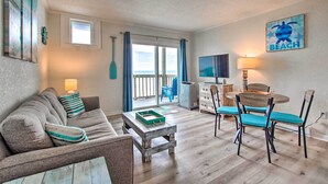 A living room with a sofa, coffee table, and chairs, a TV, a lamp, and a painting on the wall. - North Topsail Beach Condo w/ Balcony! (Sneads Ferry)