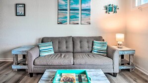 A living room with a grey sofa, striped pillows, a wooden coffee table, and a framed artwork above. - North Topsail Beach Condo w/ Balcony! (Sneads Ferry)