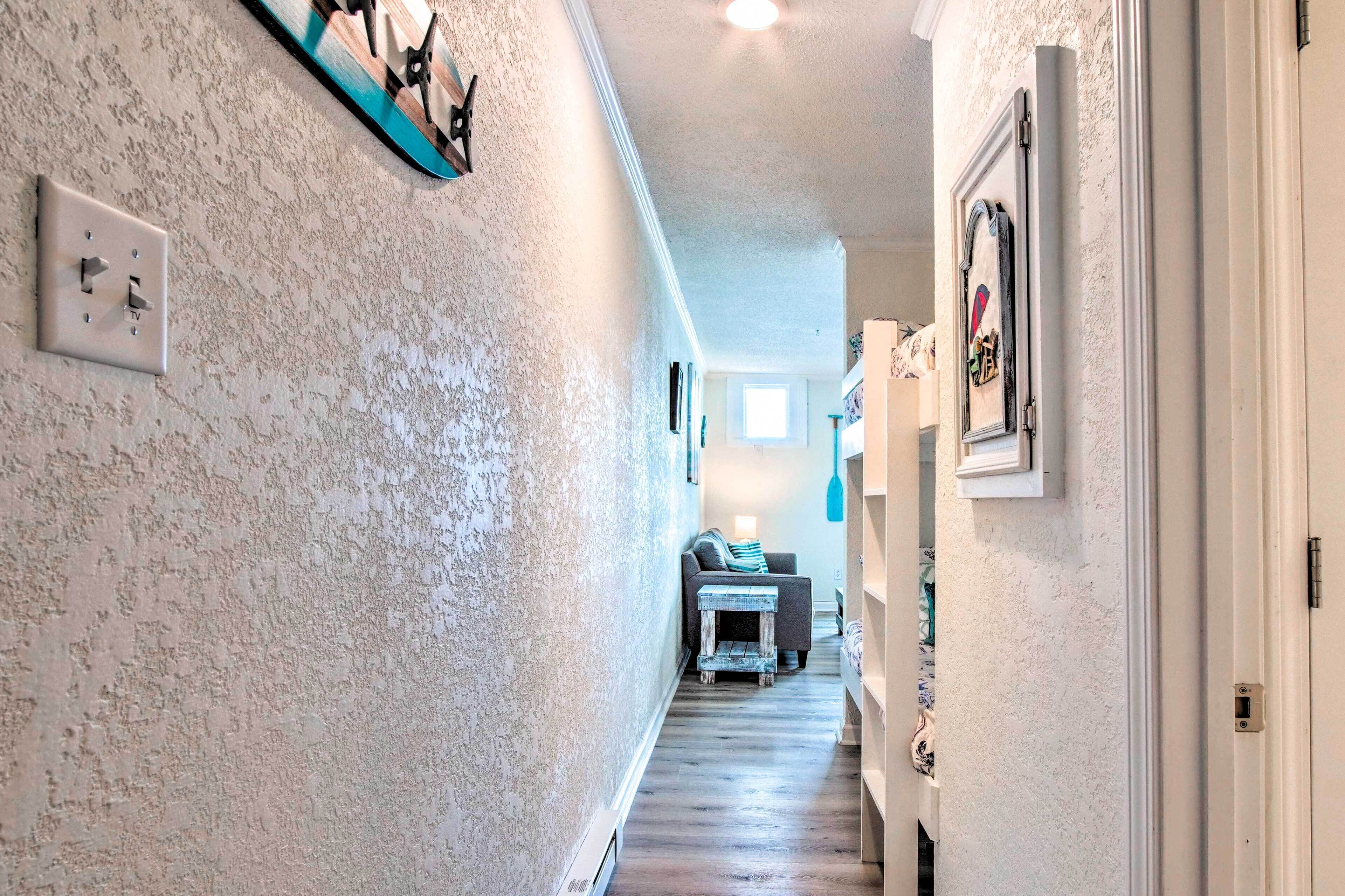 A hallway with textured walls, a light switch, a small table, and a couch in the distance.