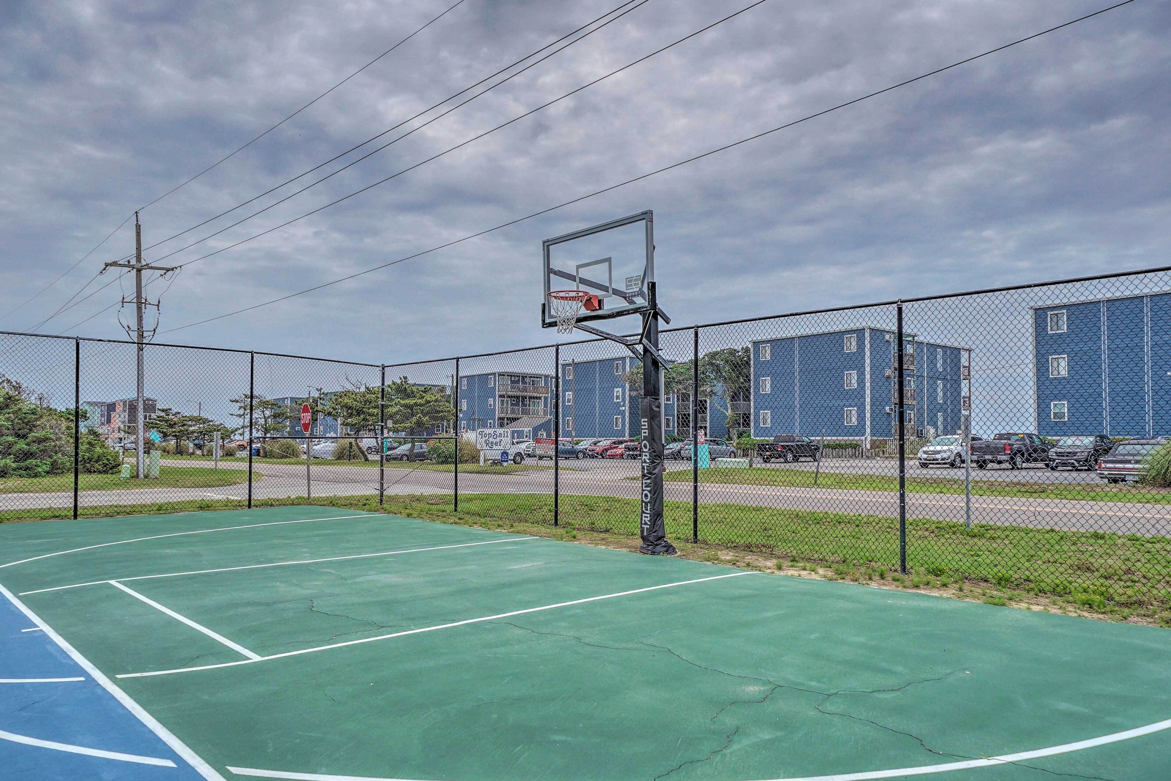 Ein Basketballplatz im Freien mit einem Maschendrahtzaun, einem Basketballkorb und einem Stoppschild im Hintergrund.