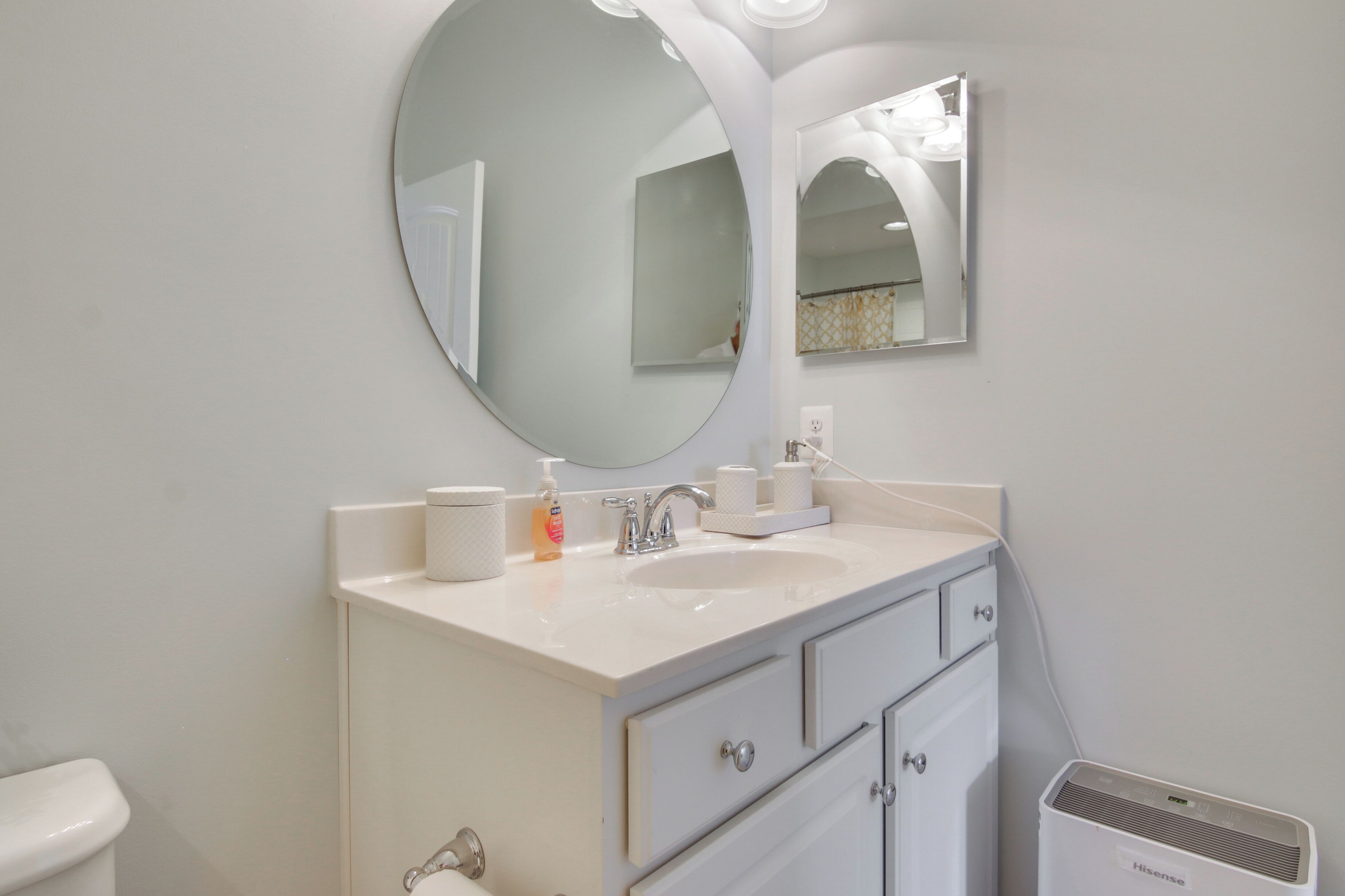 A bathroom with a round mirror, a sink, a toilet, and a wall-mounted heater.