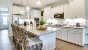 A modern kitchen with white cabinetry, a central island, pendant lighting, and a stainless steel refrigerator.