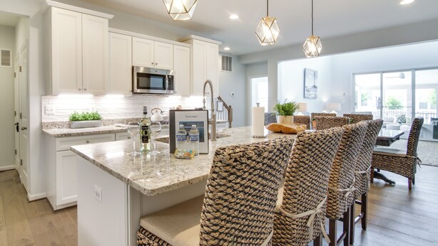 A modern kitchen with white cabinets, a built-in microwave, and a central island with bar stools.